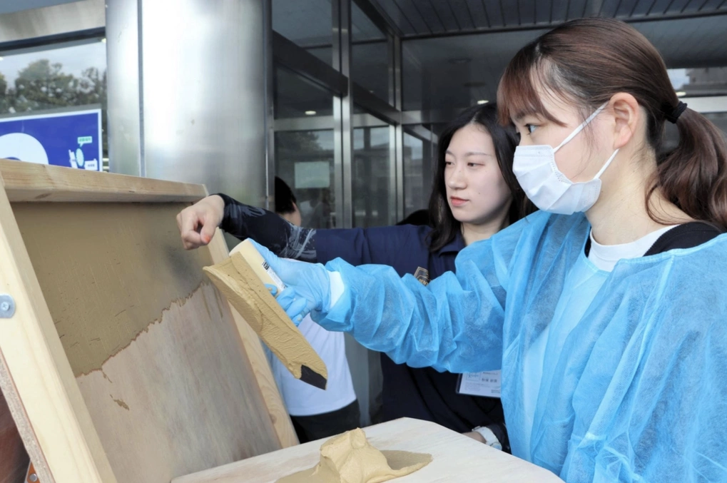 Một thợ trát vữa hướng dẫn sinh viên Đại học Tohoku Bunka Gakuen (Nhật Bản) cách trát vữa lên tường. Ảnh: Kahoku Shimpo